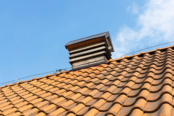 Old orange ceramic roof tiles. Tiled roof texture. Blue sky over the house. Chimney  wooden vent structure at the rooftop's peak. Lightning rod running along the roof.