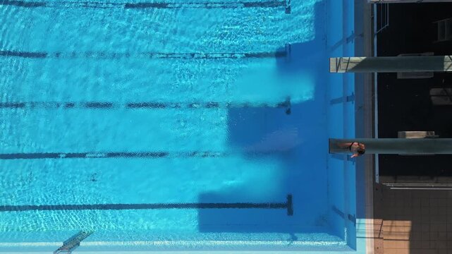 Drone footage capturing a diver mid-air performing a tuck dive above a clear blue pool, with stunning reflections and precise timing. Perfect for sports, aerial, and aquatic-themed projects