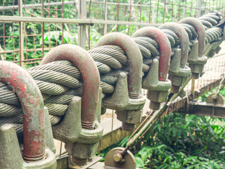 Naklejka premium Sturdy metal cable clamps securing strong tension lines outdoors. Rusty yet reliable cable clamps supporting outdoor suspension. Strong steel wire clamps tightly securing industrial cables.