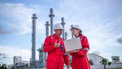 Engineers wearing safety gear, including hard hats examining survey a large blueprint tablet...