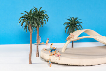 Vacationers relaxing on a flip flop sandal on an oasis, miniature figures scene, close up