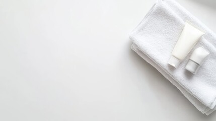 A folded white towel rests on the edge of a rectangular bathtub, accompanied by a small cream tube, all set against a bright, pristine white background