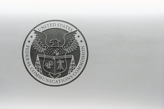 Federal Communications Commission (FCC) logo against a white wall.