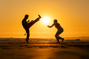 Athletes training capoeira at sunset on the beach