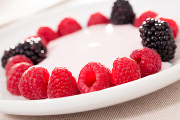 Fresh raspberries and blackberries laid out on a white plate in circle with yogurt