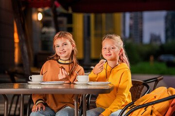 Two schoolgirls are sitting at a table in a city open-air cafe.