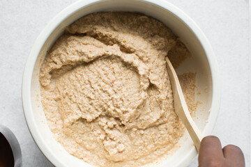 Overhead of moi moi mixture in a white ceramic bowl, top view of nigerian bean pudding being mixed, process of making nigerian moi moi