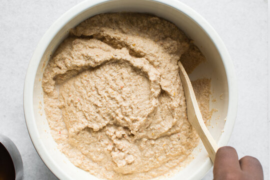 Overhead of moi moi mixture in a white ceramic bowl, top view of nigerian bean pudding being mixed, process of making nigerian moi moi