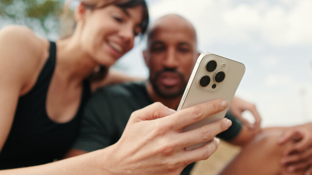 Close-up of athletic couple in love relaxing and using smartphone, focus on the mobilephone