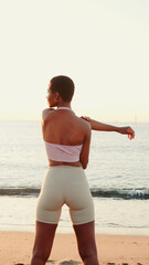 Young active sporty woman kneading her back by the sea, stretching routine and healthy lifestyle...