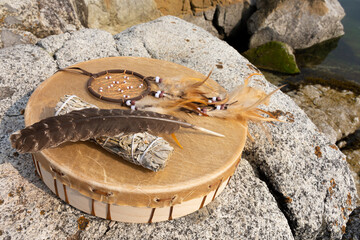 An image of a handmade leather meditation drum with sacred feather and white sage smudge stick.