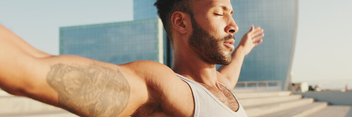 Close up, young bearded male athlete doing workout, stretching on the embankment, panorama