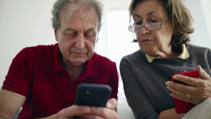 Elderly couple focused on smartphones, exploring apps together, engaged in modern technology, digital literacy, senior lifestyle, bonding over gadgets, casual indoor setting, learning new skills