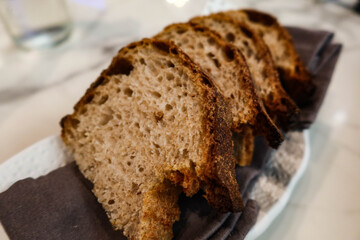 close up of four pieces of sliced wheat grain Sourdough gluten Bread on a grey tissue on a white plate in a marble pattern table