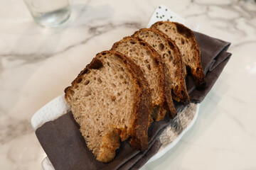 close up of four pieces of sliced wheat grain Sourdough gluten Bread on a grey tissue on a white plate in a marble pattern table