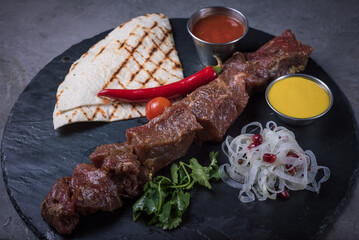 Raw beef shashlik with lavash, onion with spices and sauces on a black stone board, side view close-up