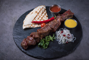 Raw beef shashlik with lavash, onion with spices and sauces on a black stone board, side view close-up