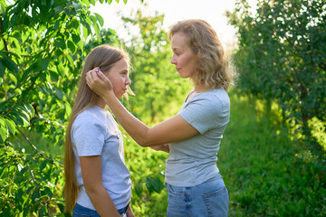 mother and teenage girls with long blond hair spend time together in the sunlit park