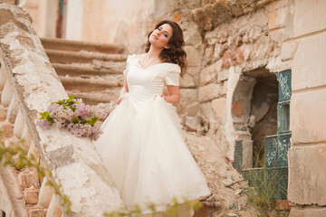 Obraz premium THE EUROPEAN BEAUTIFUL BRIDE WITH THE BEAUTIFUL DARK HAIR WITH THE BOUQUET ON THE BACKGROUND OF THE GREAT BRUSH OF LILAC