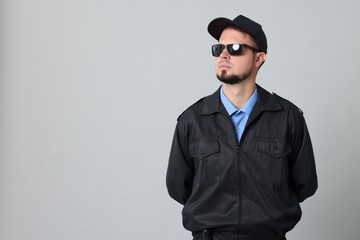 Security guard in uniform and sunglasses on grey background, space for text