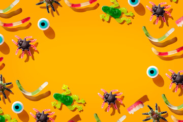 Halloween frame of scattered sweet colorful assorted gummy candy with long shadows on a orange background. Halloween party border. Copy space. Banner. Space for text. Top view