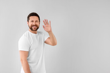 Fototapeta premium Cheerful man waving on light background. Space for text