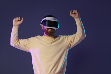 Smiling man using virtual reality headset on dark purple background
