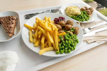 Meatballs with french fries, green peas, bechamel sauce and cranberry jam, meat balls on white plate