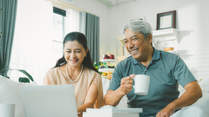 Two retired senior couple watching media on laptop and laughing having fun talking about retirement...