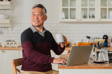 Asian male man gray hair senior retired enjoying coffee breakfast at kitchen counter weekend while reading newspaper Smiling senior man with book while sitting in kitchen at home healthy lifestyle