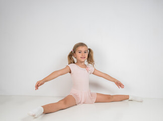 Little girl ballerina in pink dress doing gymnastic exercises.