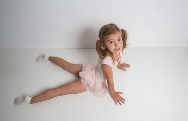 Little girl ballerina in pink dress doing gymnastic exercises.