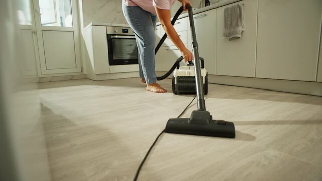 A woman vacuums the kitchen floor with a vacuum cleaner. Cleaning and cleanliness at home with the help of equipment. High quality 4k footage