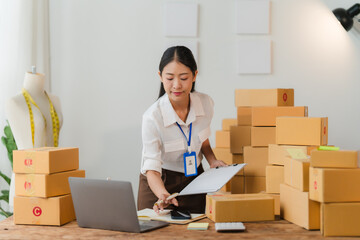 E-commerce Hustle: Asian SME entrepreneur meticulously manages online orders in her home office, surrounded by shipping boxes, embodying the spirit of female-led small businesses. 