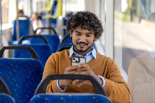 Man sitting on bus using smartphone with a smile. Casual setting in public transport with blue seats and window light. Engaged and relaxed moment captured.