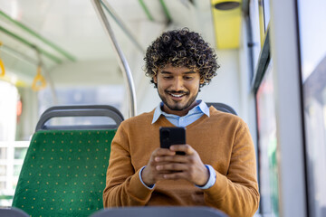 Young man sitting on bus using smartphone, smiling and engaged in digital content. Casual attire...