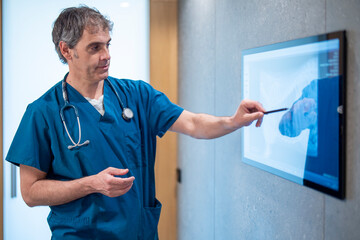 A veterinarian in blue scrubs attentively examines an X-ray image displayed on a digital screen, using a stylus to highlight key areas. The scene takes place in a modern veterinary clinic.