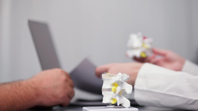 Close-up of a doctor’s hands demonstrating a detailed medical explanation using a spine model. Ideal for showcasing expert knowledge, patient education, and healthcare professionalism.