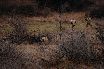 Group of armed soldiers spread out across open terrain during a tactical operation