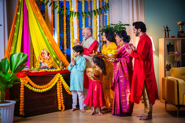 Indian Asian family performing Ganesh Puja at home in traditional attire, celebrating with devotion