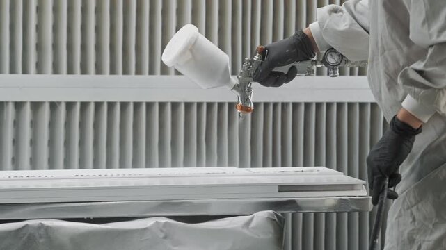 Close-up of the application of white paint from a spray gun on a part in an industrial setting. Close up. Slow motion.