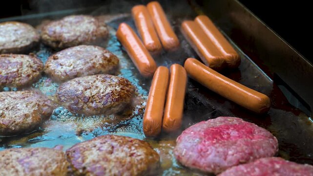 Hot Dogs and Hamburgers grilling on a Propane fired Flattop grill.  Cooking outside in Summer is an American Family Tradition.  Good Food Sizzling.