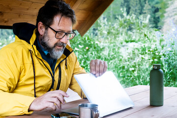 Mature freelance opening laptop ready to work in outdoors alternative nature office workplace. Traveler lifestyle. Remote worker everywhere with roaming 5g connection data. Adventure lifestyle people