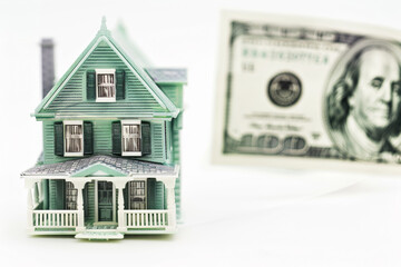 A house and a dollar bill are shown in front of each other