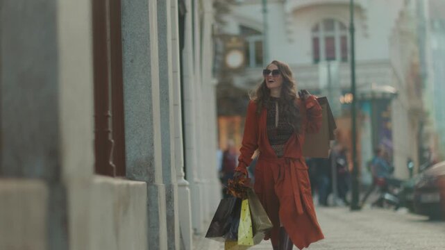 Hello september. smiling elegant 40 years old woman in orange trench coat with shopping bags and autumn yellow leaves in the city.