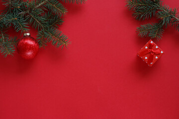 A pine branch on a red background with small gift box  and red Christmas decorations.