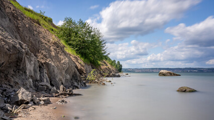 A breathtaking view of the Lake Vattern coastline near Jonkoping, Sweden. Dramatic effects of coastal erosion, with exposed layers of sedimentary rock and lush vegetation clinging to the cliff face. 