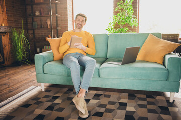 Full length photo of young guy sit couch online study write notebook dressed yellow garment spend pastime spacious house indoors room