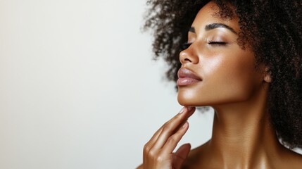 A close-up photograph of an individual with curly hair, their hand gently touching their chin, highlighting a thoughtful pose and smooth skin against a neutral background. Undefined identity.