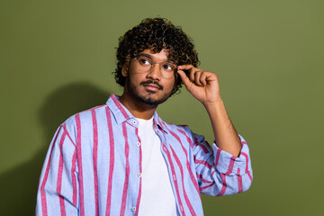 Portrait of confident serious arabian businessman in striped casual shirt touching expensive glasses isolated on khaki color background